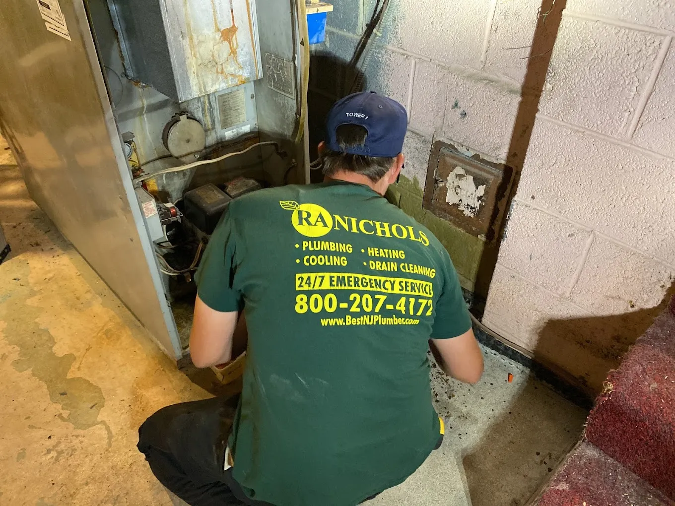 A man wearing a green shirt works on fixing a furnace