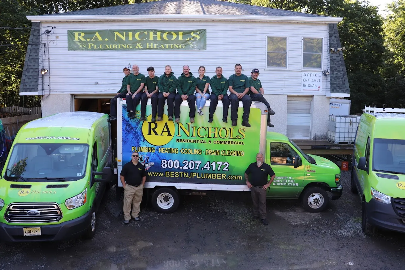 A group of men stands together in front of green trucks